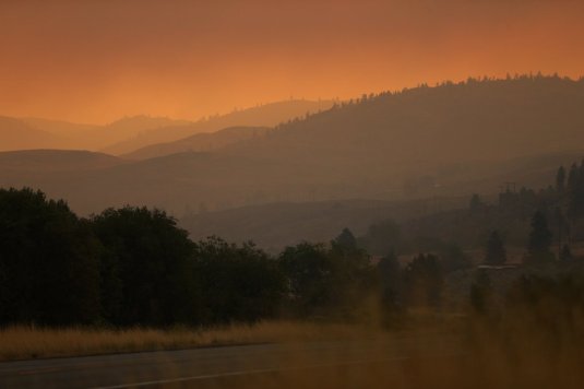 The sun barely illuminates the land under a thick fog of red smoke as seen from Highway 97 just south of Okanogan Friday August 21, 2015.